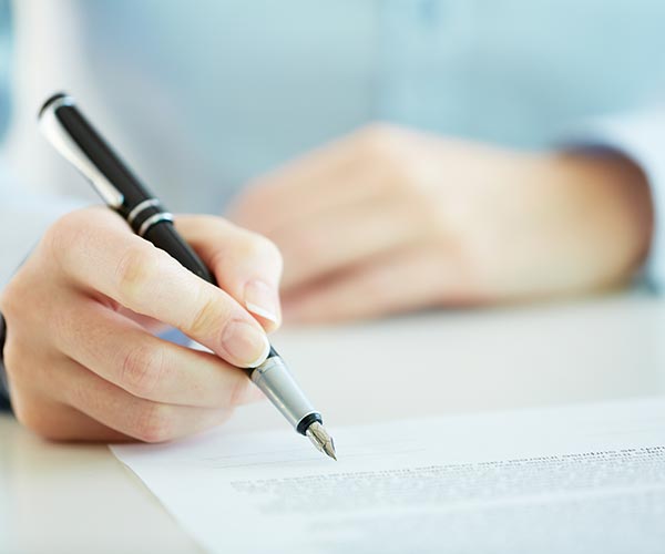 person holding pen writing on a form